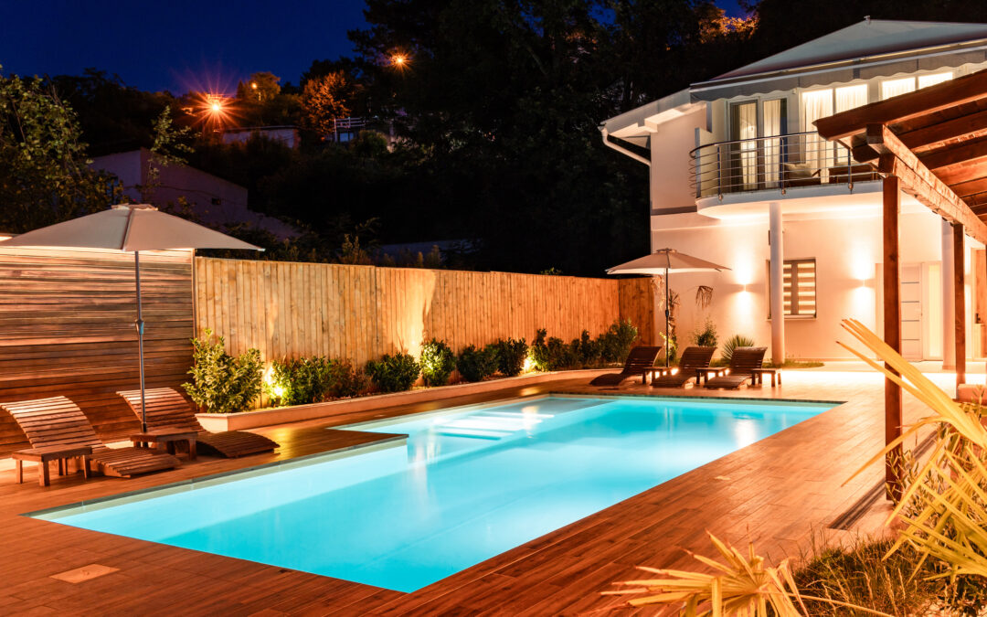 An elegant backyard with illuminated swimming pool and modern house at night for landscape-lighting-maryland blog.